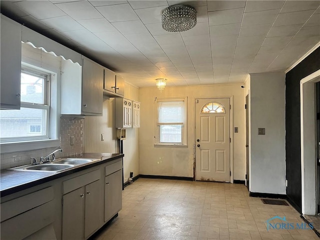 kitchen featuring a wealth of natural light, decorative backsplash, dark countertops, and a sink