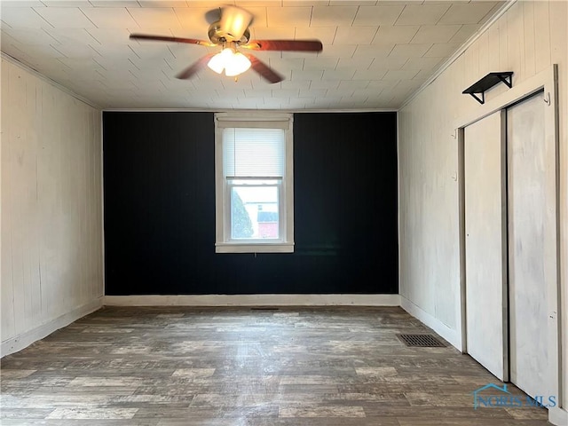 unfurnished bedroom featuring wood finished floors, visible vents, baseboards, ceiling fan, and ornamental molding