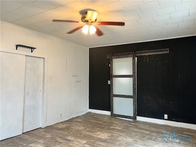 empty room featuring a barn door, wood finished floors, baseboards, and ceiling fan