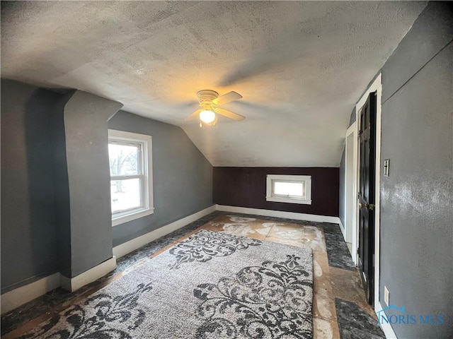 additional living space with lofted ceiling, a textured ceiling, a healthy amount of sunlight, and a ceiling fan