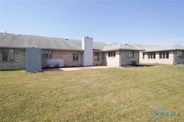 rear view of property with a patio, a lawn, brick siding, and a chimney