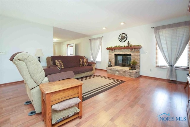 living room with a brick fireplace, baseboards, light wood-type flooring, and a wealth of natural light