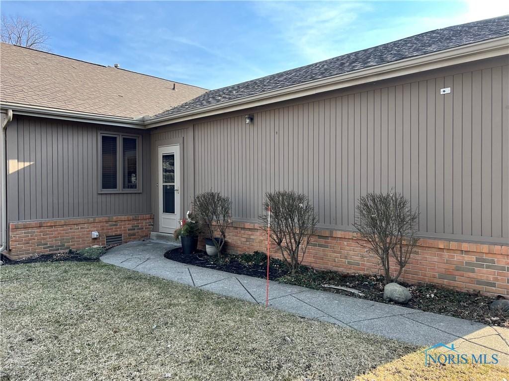 property entrance featuring a lawn, roof with shingles, and crawl space