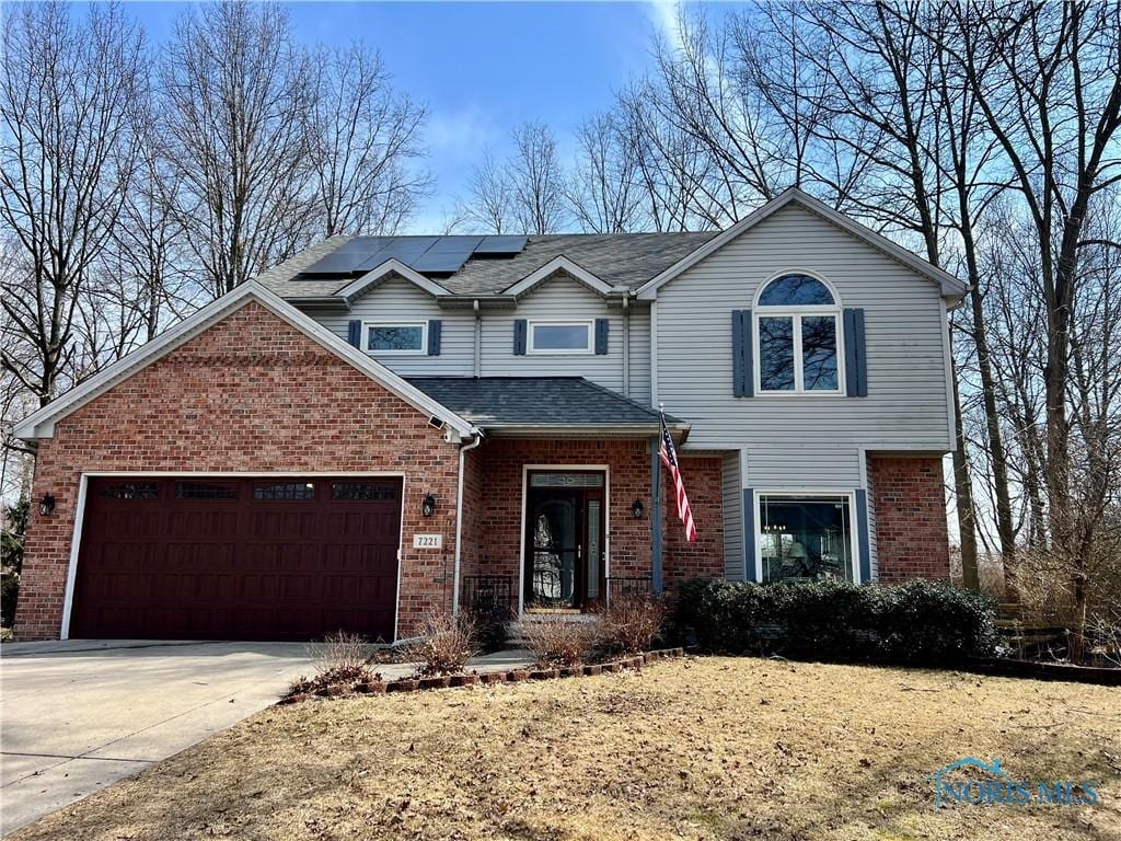 traditional-style home featuring driveway, roof with shingles, an attached garage, brick siding, and solar panels