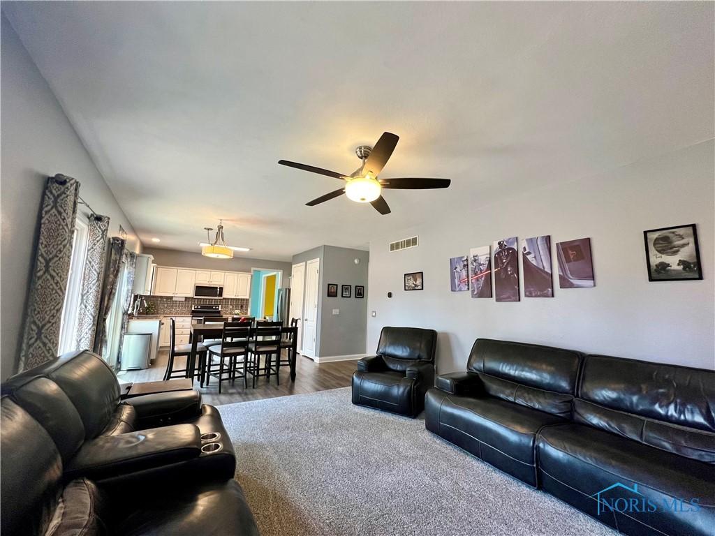 living room featuring dark wood finished floors, visible vents, baseboards, and a ceiling fan