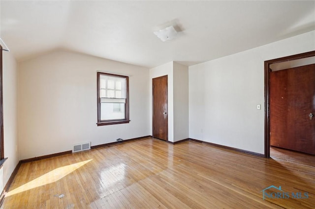 unfurnished room featuring vaulted ceiling, visible vents, baseboards, and hardwood / wood-style flooring