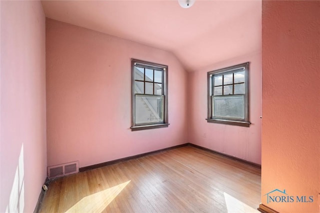 spare room featuring vaulted ceiling, wood finished floors, visible vents, and baseboards