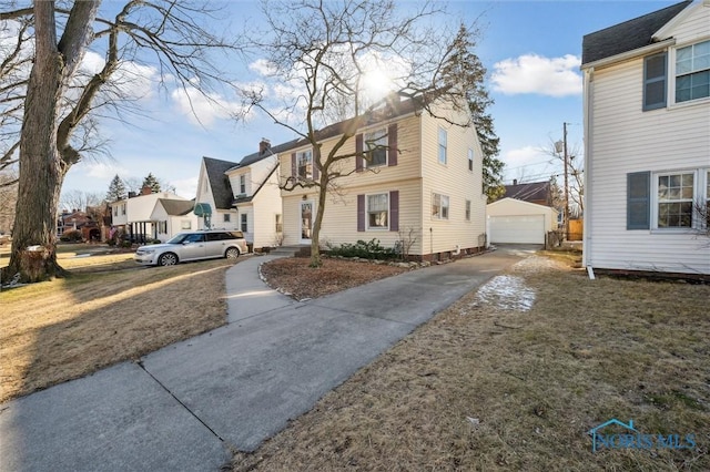 view of front of home with a residential view, concrete driveway, a chimney, a garage, and an outbuilding