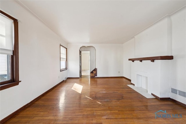 unfurnished living room with hardwood / wood-style floors, visible vents, baseboards, and arched walkways