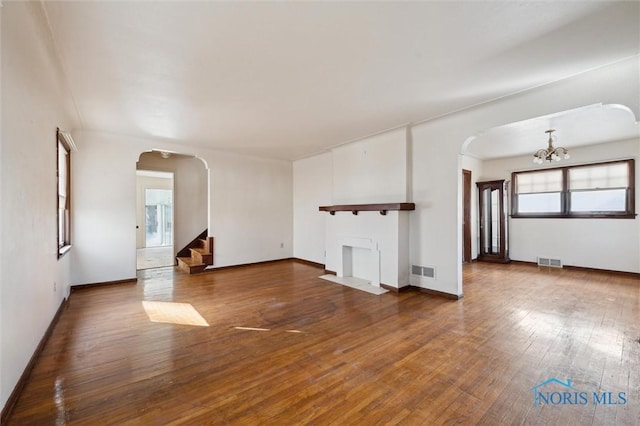 unfurnished living room featuring arched walkways, visible vents, a notable chandelier, and hardwood / wood-style flooring