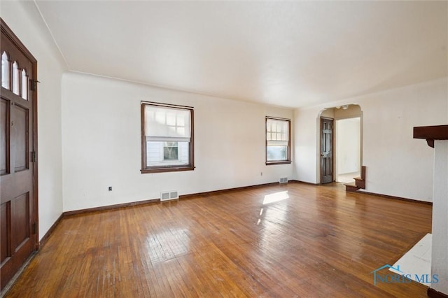 unfurnished living room featuring arched walkways, visible vents, baseboards, and hardwood / wood-style floors