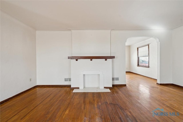 unfurnished living room featuring baseboards, arched walkways, and wood finished floors