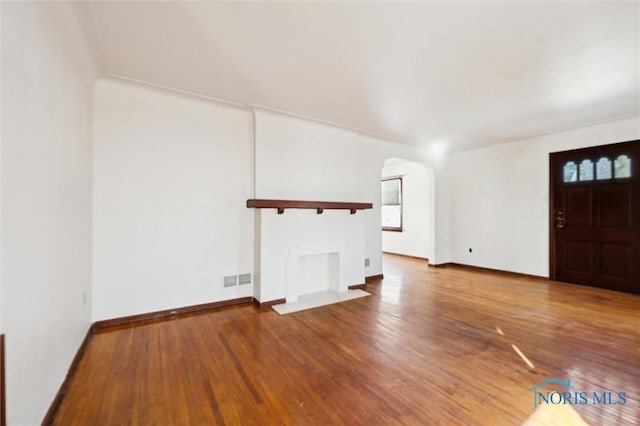 unfurnished living room featuring baseboards, arched walkways, a healthy amount of sunlight, and hardwood / wood-style floors