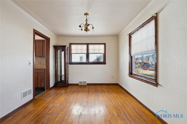 empty room with a chandelier, visible vents, and hardwood / wood-style flooring