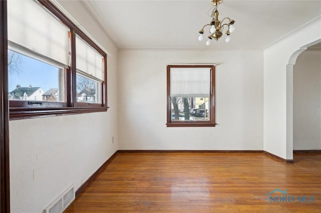 spare room with wood finished floors, visible vents, baseboards, an inviting chandelier, and arched walkways