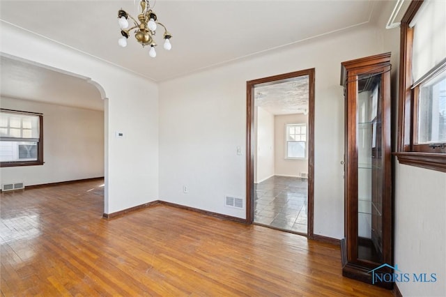 spare room with visible vents, arched walkways, an inviting chandelier, and wood-type flooring