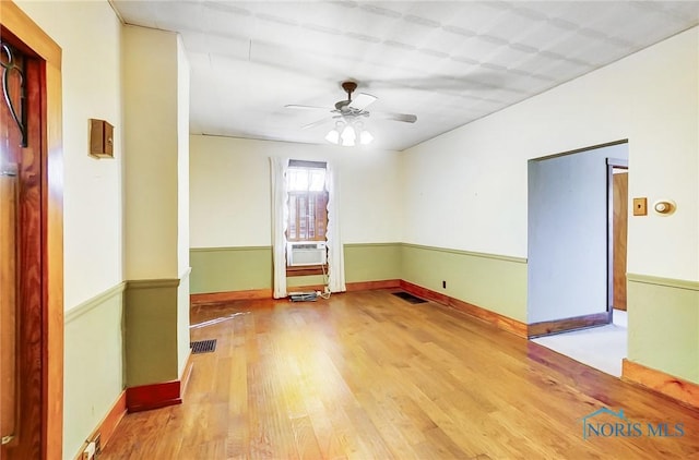 empty room featuring visible vents, a ceiling fan, wood finished floors, cooling unit, and baseboards