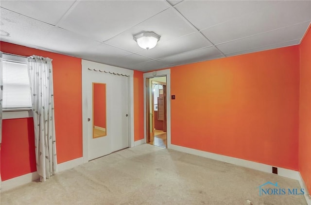 spare room featuring carpet, baseboards, and a drop ceiling