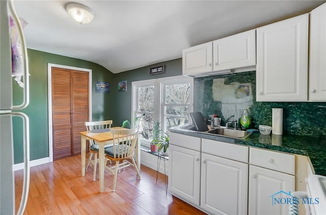 kitchen featuring backsplash, light wood-type flooring, freestanding refrigerator, white cabinetry, and a sink