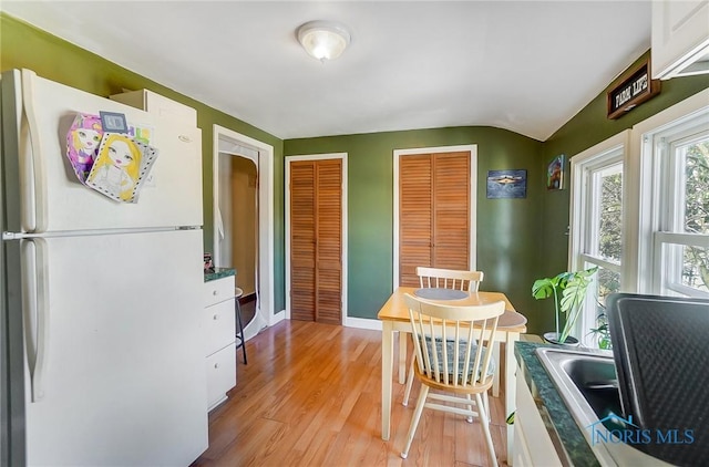 dining area with vaulted ceiling, baseboards, and light wood finished floors