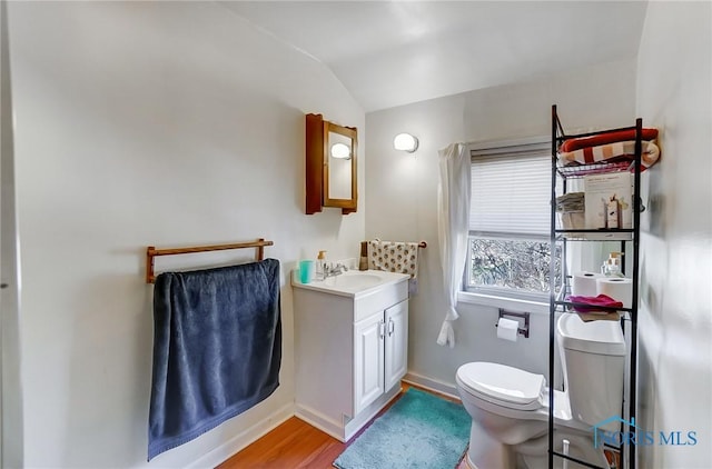 half bathroom featuring baseboards, toilet, lofted ceiling, wood finished floors, and vanity