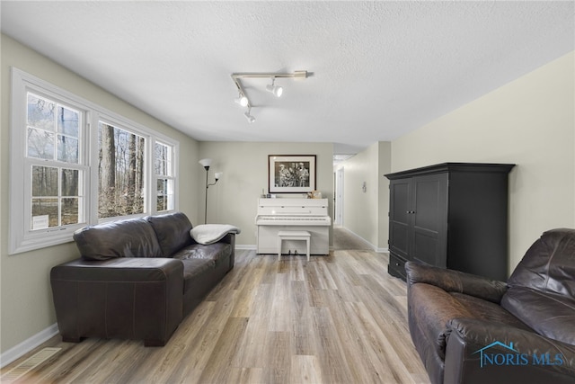 living room featuring light wood-type flooring, visible vents, baseboards, and a textured ceiling