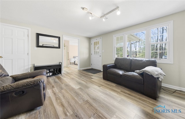 living room featuring track lighting, baseboards, and light wood finished floors