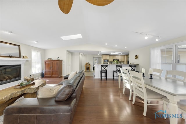 living room featuring lofted ceiling with skylight, dark wood-type flooring, a glass covered fireplace, and rail lighting