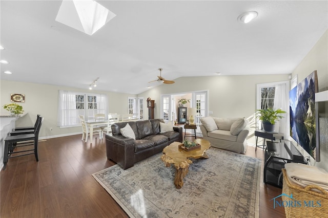 living room featuring baseboards, lofted ceiling with skylight, dark wood-style floors, and a ceiling fan