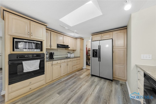 kitchen featuring black appliances, light brown cabinets, under cabinet range hood, light wood-style floors, and a skylight