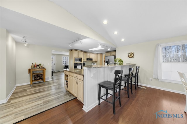 kitchen featuring a kitchen breakfast bar, wood finished floors, appliances with stainless steel finishes, a peninsula, and lofted ceiling