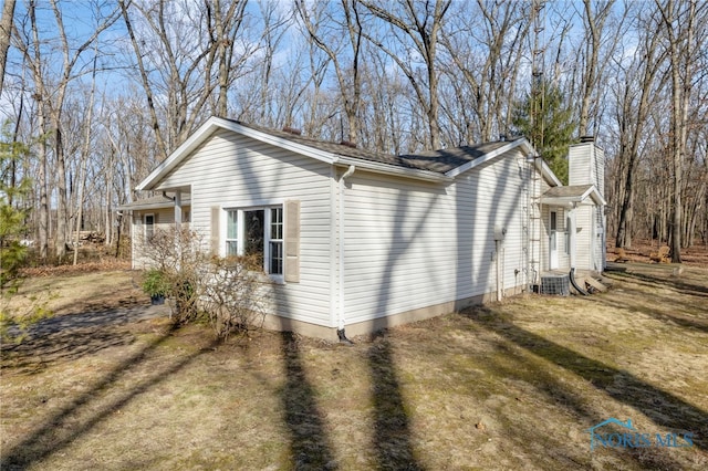 view of side of home featuring central air condition unit, a lawn, and a chimney