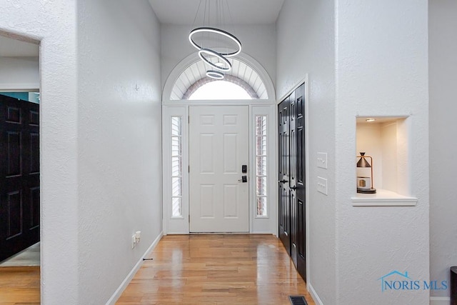 foyer with light wood finished floors, a chandelier, visible vents, and baseboards