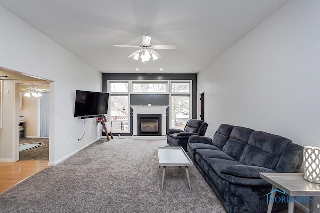 carpeted living area with a glass covered fireplace, baseboards, and a ceiling fan