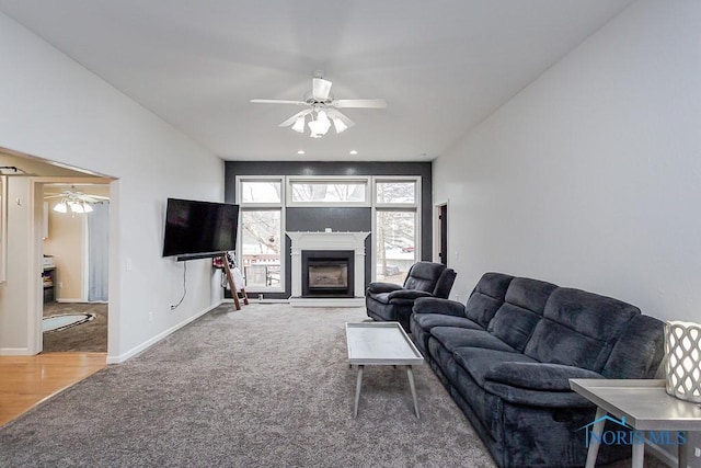 carpeted living room featuring baseboards, a ceiling fan, wood finished floors, and a glass covered fireplace