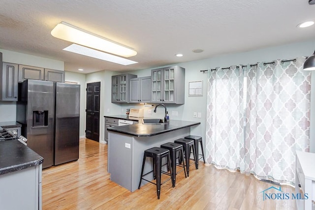 kitchen with dark countertops, a sink, gray cabinetry, and stainless steel fridge with ice dispenser