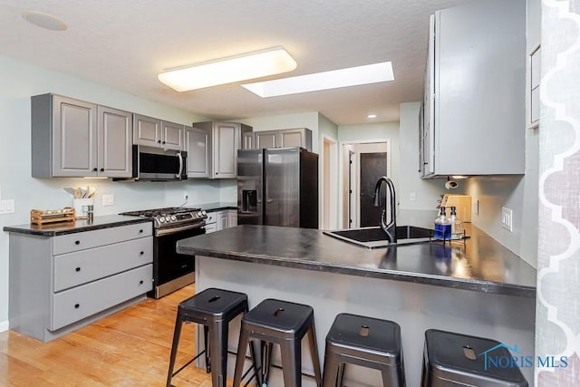 kitchen with a peninsula, a skylight, gray cabinetry, a sink, and appliances with stainless steel finishes