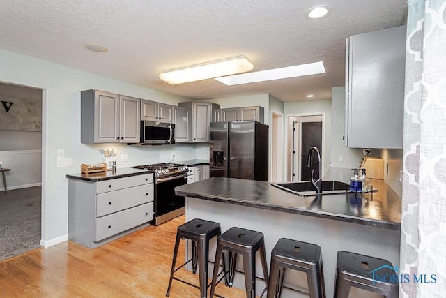 kitchen with a peninsula, dark countertops, gray cabinetry, appliances with stainless steel finishes, and a sink