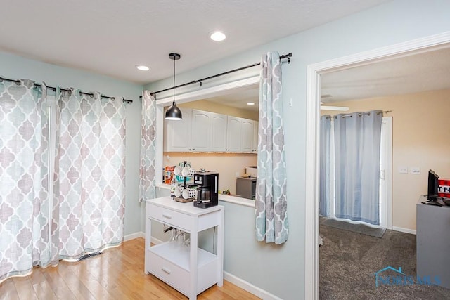 kitchen featuring baseboards, light wood finished floors, recessed lighting, white cabinetry, and decorative light fixtures