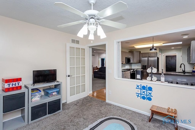 carpeted living room with ceiling fan, visible vents, a sink, french doors, and baseboards
