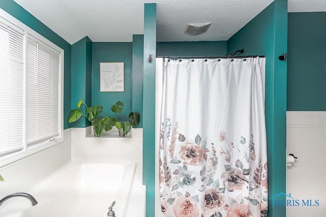 bathroom featuring a shower with curtain, a garden tub, and a textured ceiling