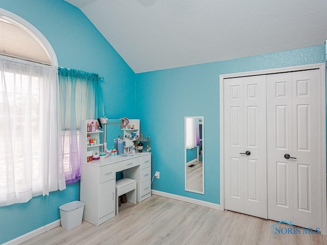 bedroom with a closet, baseboards, light wood-style floors, and vaulted ceiling