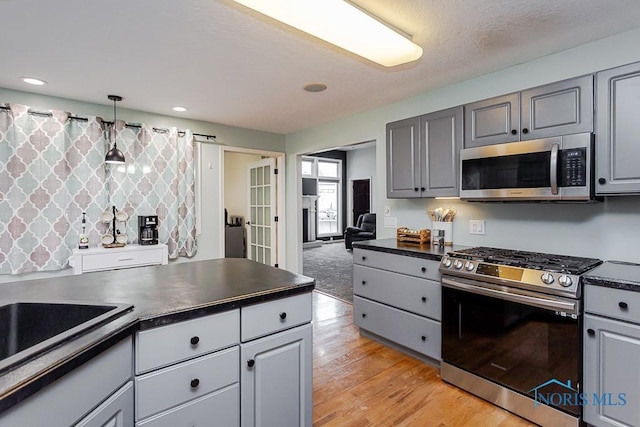 kitchen featuring dark countertops, gray cabinetry, stainless steel appliances, light wood-style floors, and a textured ceiling