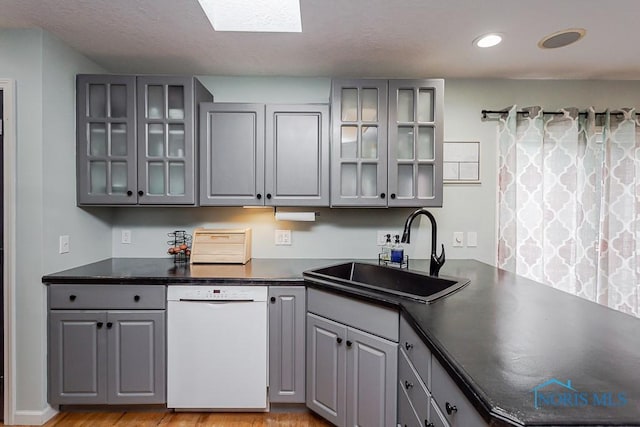 kitchen featuring dark countertops, a sink, gray cabinets, and white dishwasher