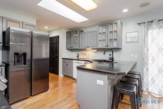 kitchen with dark countertops, a peninsula, gray cabinets, and a sink