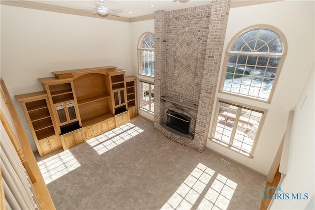 carpeted living room featuring visible vents, ornamental molding, a high ceiling, a brick fireplace, and ceiling fan