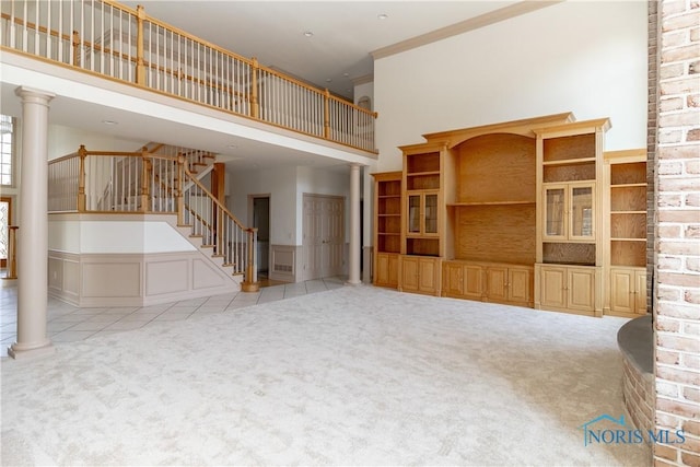 unfurnished living room featuring decorative columns, carpet, and stairs