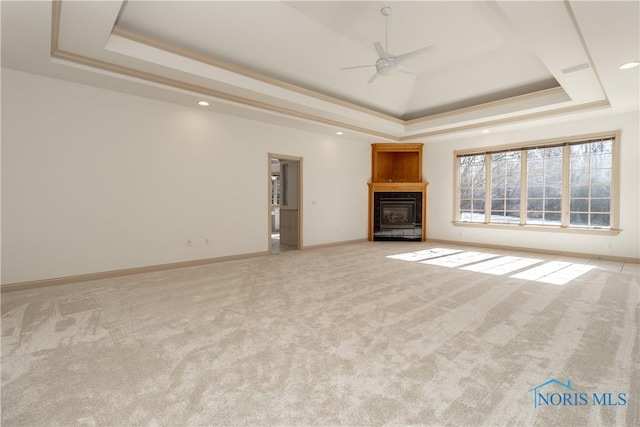 unfurnished living room with a tray ceiling, light colored carpet, a glass covered fireplace, and a ceiling fan