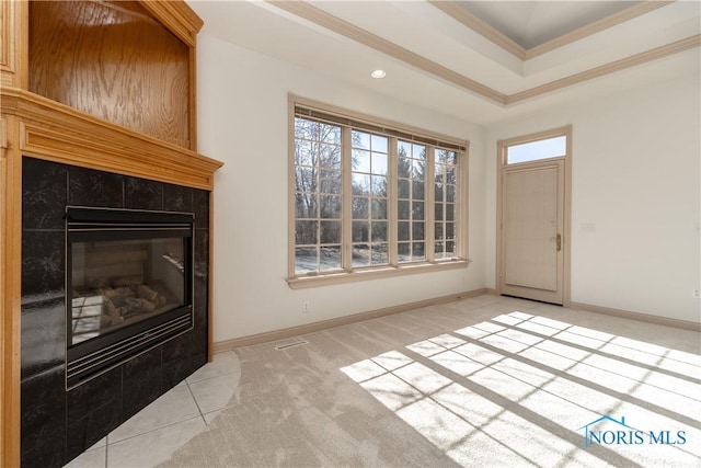 unfurnished living room featuring a raised ceiling, a fireplace, crown molding, baseboards, and light colored carpet