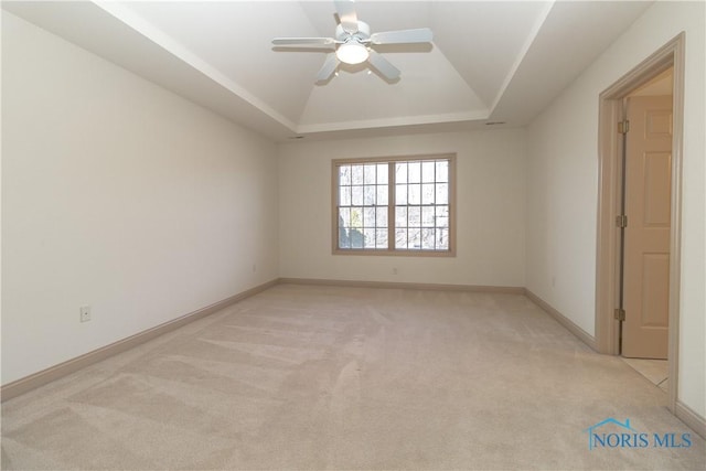 spare room with a tray ceiling, light carpet, baseboards, and a ceiling fan